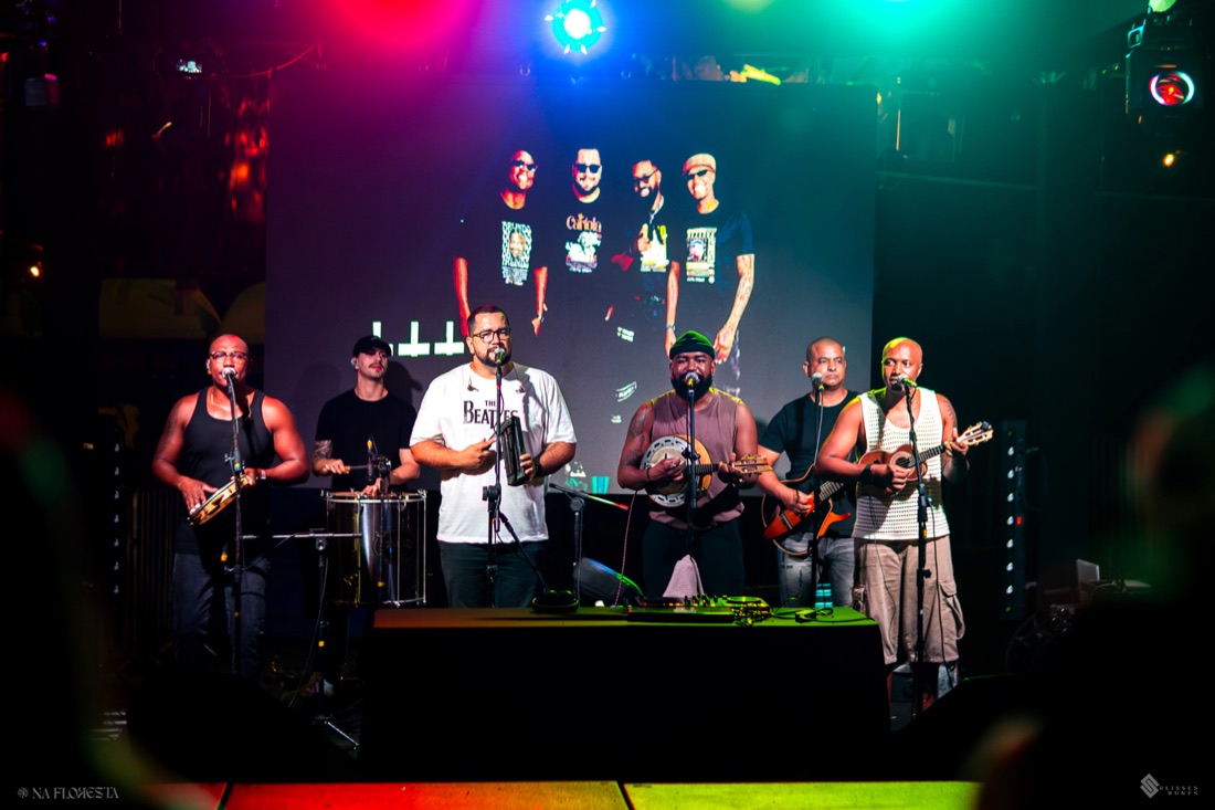 O grupo tocando no palco sob a luz colorida da casa