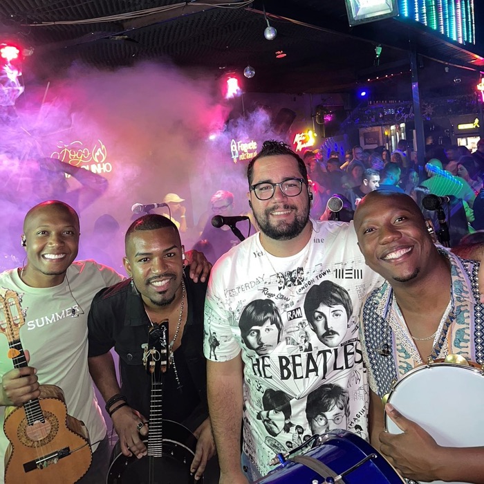 O grupo no palco de uma casa noturna, com o público atrás